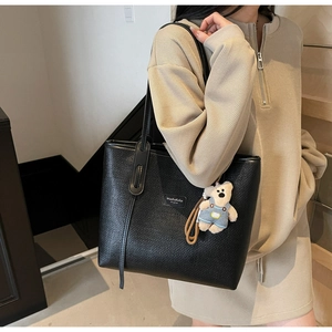 Close-up of black woven tote bag with a cute bear charm on a beige knit sweater