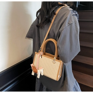 Détail du sac bandoulière tissé avec poignées en cuir marron et pendentif cheval