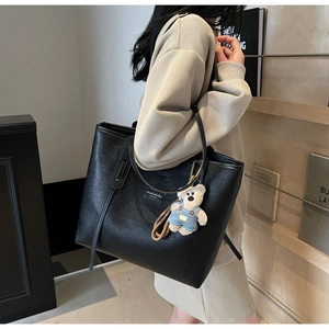Detail of black woven tote bag with cute plush bear charm and brand label on strap