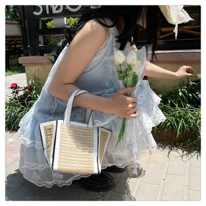 Outdoor shot of a woven straw tote bag with white faux leather trim held by a model in a garden
