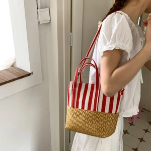 Detail of red striped canvas and straw woven tote bag shown on model's shoulder