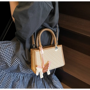Détail d'un sac à main carré tissé beige avec des poignées brunes et un charme pégase