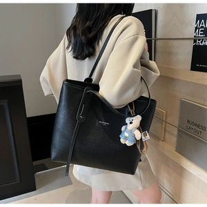 Detail of black pebbled leather tote bag with a cute bear plush keychain and brand tag
