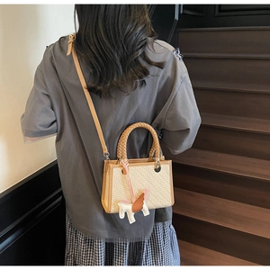 Mannequin portant un sac bandoulière en paille avec garniture en cuir brun et breloque