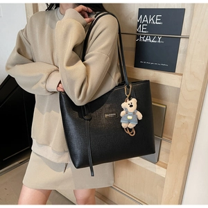 Macro view of textured black tote bag with a cute bear plush charm and brand leather patch