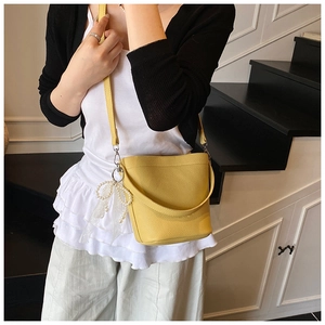 Close-up of a yellow pebbled leather bucket bag with a white pearl lace bow pendant
