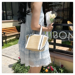 Detail of woven straw tote bag featuring white leather trim and black piping accents