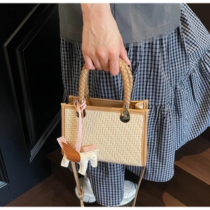 Gros plan du sac à main en paille tressée avec garniture en cuir brun et charme Pégase