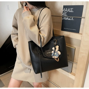 Close-up of black woven tote bag with metallic logo plate and cute teddy bear charm