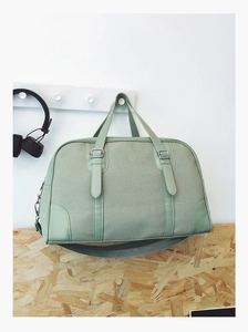 Close-up of light green canvas travel bag with leather handles on a wall hook