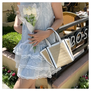 Detail of woven straw tote bag with white leather trim held in a bright garden