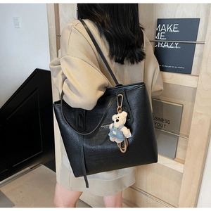 Detail of black woven leather tote bag with cute bear charm and logo patch on the shoulder