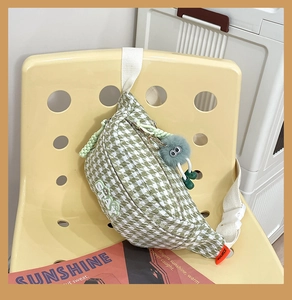Détail du sac bandoulière pied-de-poule vert avec peluche sur une chaise jaune