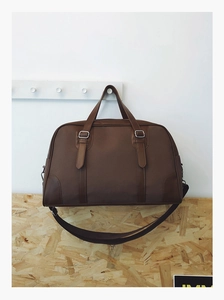 Close-up of brown travel bag featuring fabric texture, leather corners, and adjustable strap