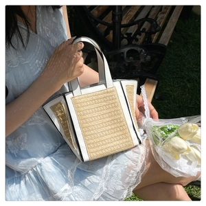 Straw and white leather tote bag shown in outdoor setting with a blue floral dress