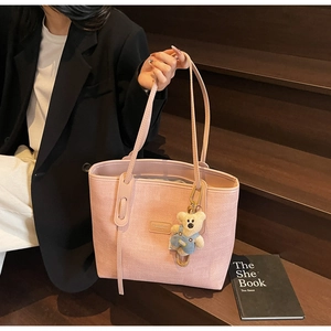 Pink woven tote bag with a cute plush bear charm and brand logo plate in detail view
