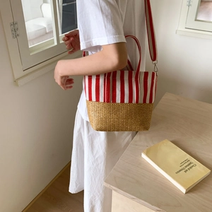 Detail of red stripe canvas and woven straw tote bag worn by a model in casual setting