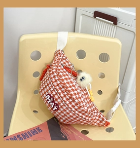 Détail du sac bandoulière orange à motif pied-de-poule avec écusson et pompon blanc
