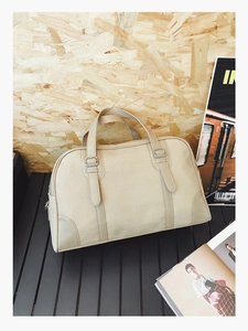 Close-up of beige canvas handbag with leather拼接 details and metallic buckle straps