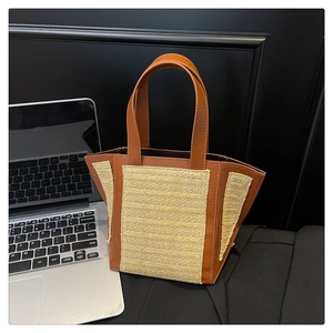 Detail of woven straw panels and brown leather handles on a trapezoid tote bag