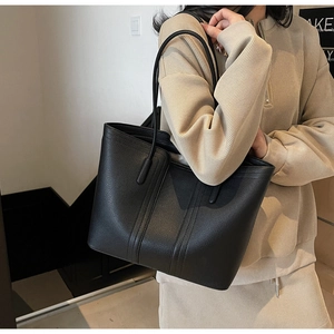 Gros plan d'un sac cabas noir en cuir grainé porté à l'épaule dans un décor moderne chic