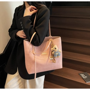 Pink woven tote bag featuring a cute teddy bear pendant and a sleek leather shoulder strap