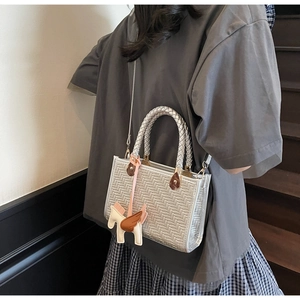 Détail d'un sac à main tissé argenté avec un charm de pégase rose sur la poignée
