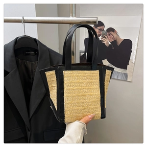Close-up of woven straw tote bag with black leather stitching and dual top handles