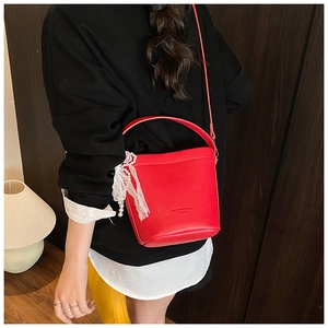 Detail view of a red bucket bag with lace bow and pearl pendant on a model's shoulder