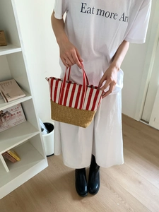 Close-up of red and white striped tote bag with woven straw bottom panel and fabric handles