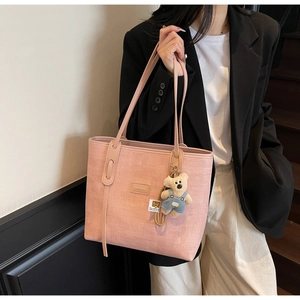 Detail of light pink woven tote bag featuring a brand patch and a cute teddy bear charm