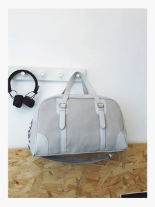 Detail of grey canvas travel bag with leather edges hanging on a white wooden wall hook