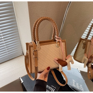 Détail du sac tressé avec bordure en cuir et breloque cheval sous une lumière chaude