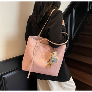 Pink textured tote bag with cute bear charm worn over the shoulder by a model