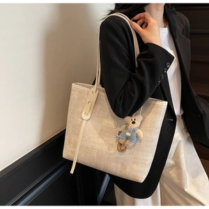 Model wearing cream woven tote bag with cute bear charm and logo detail