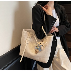 Detailed shot of an off-white textured tote bag with cute bear charm and long shoulder strap