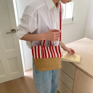 Detail of red and white striped canvas and straw woven tote bag worn by a model