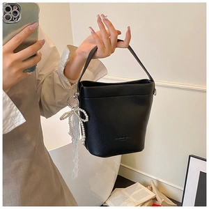 Close-up of black litchi grain leather bucket bag with a pearl lace bow pendant
