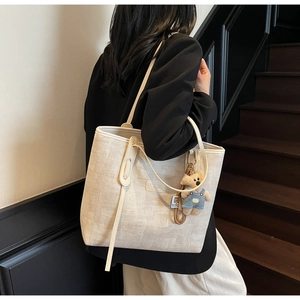 Detail view of cream woven tote bag with texture, brand plate and cute teddy bear charm