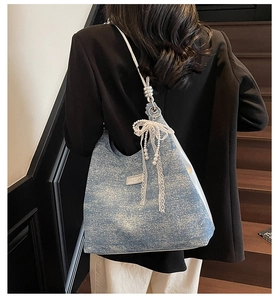 Detail of blue denim hobo bag with lace bow, pearl charm and silver chain strap