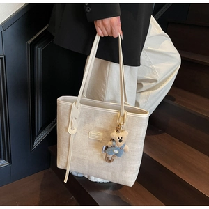 Detail of off-white woven tote bag with a cute bear pendant on a wooden staircase