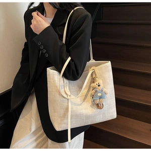Detail of beige woven tote bag with cute teddy bear charm and sturdy shoulder straps