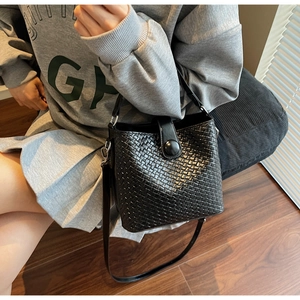 Détail du sac seau noir tressé montrant la texture et la bandoulière sur le mannequin