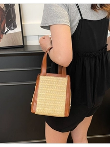 Large straw and brown leather tote bag with woven design, shown on a model's shoulder