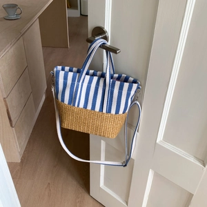 Detail of canvas tote with blue stripes and woven straw base hanging on a white door