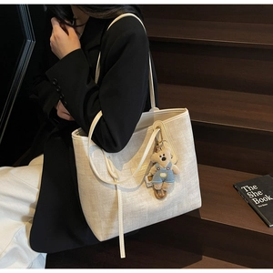 Detailed close-up of woven cream tote bag featuring a cute teddy bear plush charm