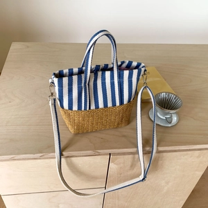 Detail of canvas striped tote with straw bottom and adjustable strap on a wooden desk