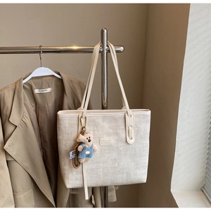 Chic cream woven tote bag with leather handles and cute bear charm on a metal stand