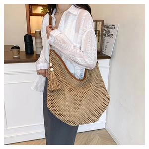 Detail der gewebten Stroh-Hobo-Tasche mit braunem Lederriemen und Boho-Quastenanhänger