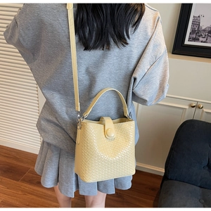 Détail du sac seau tissé jaune clair montrant sa texture, sa poignée et sa bandoulière
